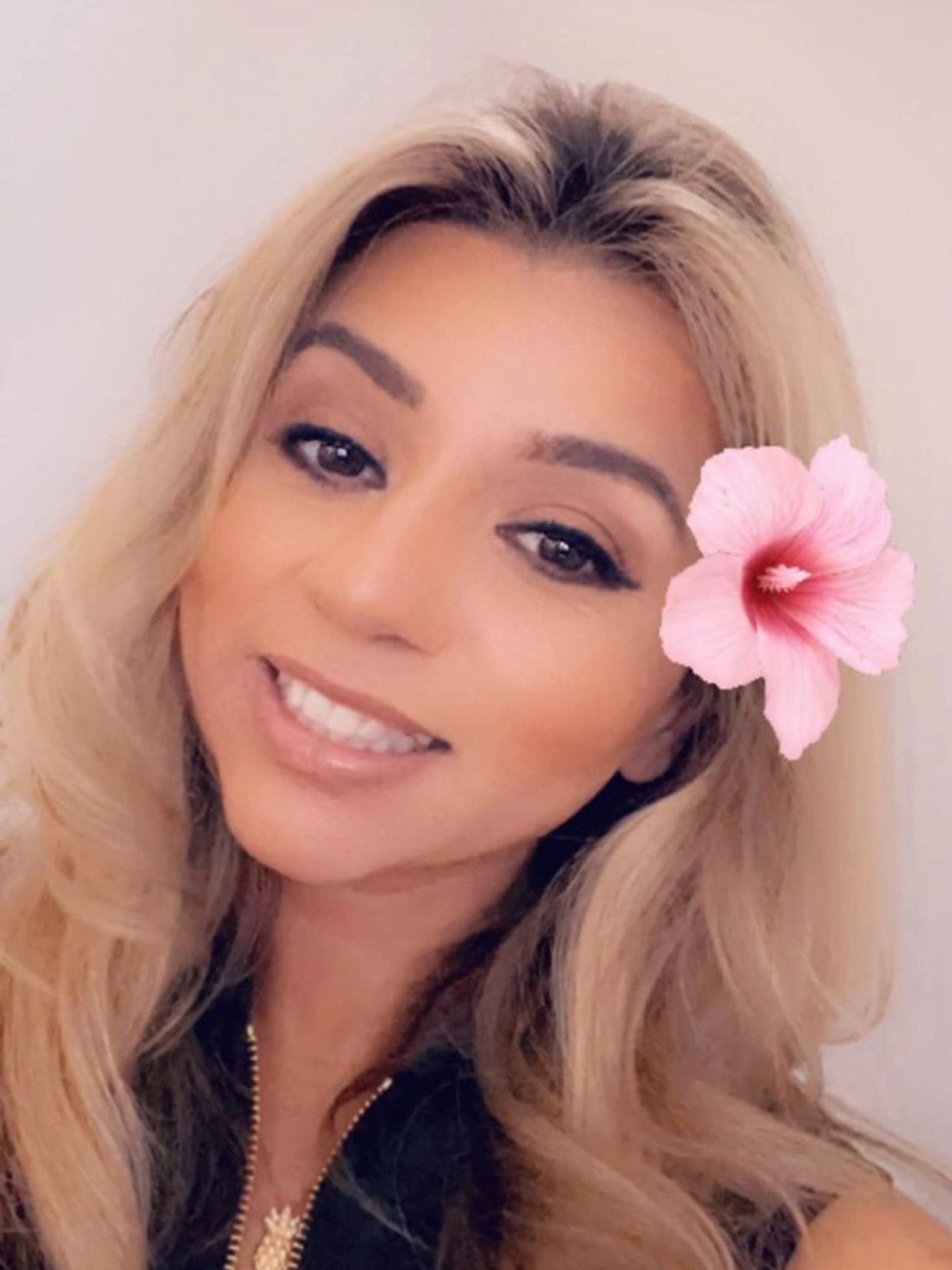 Smiling woman with blonde hair and a pink flower accessory.