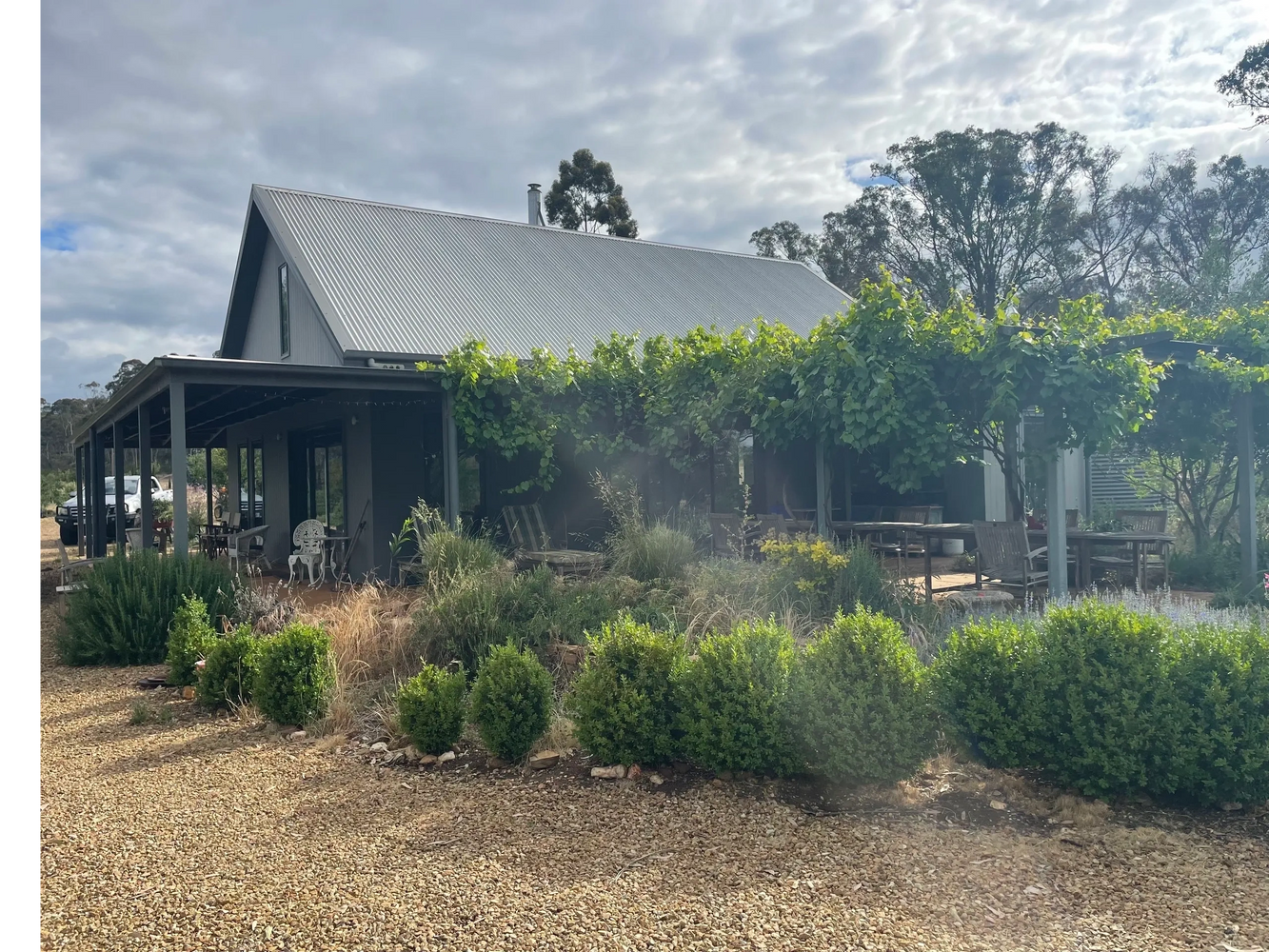 Country house with lush greenery and a gravel driveway under cloudy sky.