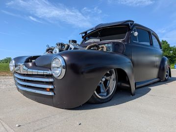 Matte black classic hot rod with exposed engine and lowered stance.