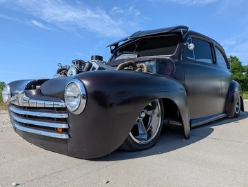 Matte black classic hot rod with exposed engine and lowered stance.