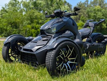 A sleek black three-wheeled motorcycle parked on grass with trees in the background.