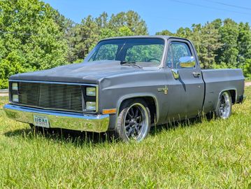 Matte gray vintage pickup truck parked on grass under a clear sky.