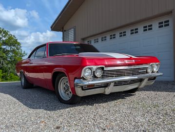 Red classic Chevrolet car parked on gravel near a garage.