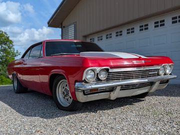 Red classic Chevrolet car parked on gravel near a garage.