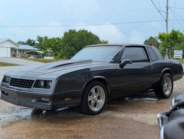 A sleek black classic coupe car parked on a wet driveway.