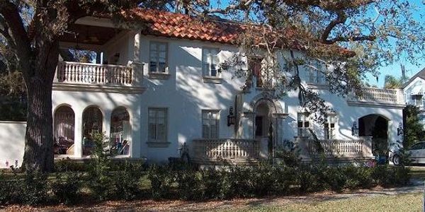 Large white Mediterranean-style house with red roof tiles and lush greenery.
