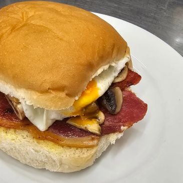 Breakfast sandwich with egg, bacon, mushrooms, and cheese on a soft bun.