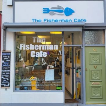 Front view of The Fisherman Cafe with a blue fish logo and menu board outside.
