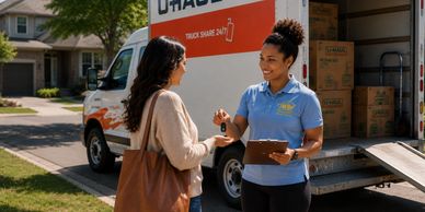 A mover hands keys to a smiling woman near a U-Haul truck.