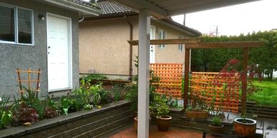 A cozy backyard patio with potted plants and garden beds under a covered area.