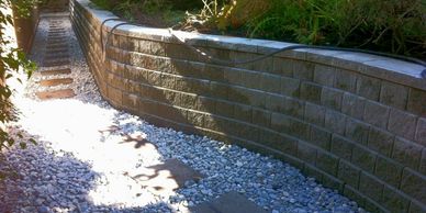 Stone path with pebbles alongside a curved retaining wall and garden hose.