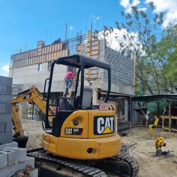 A CAT excavator at a construction site with a worker climbing on it.