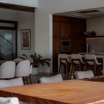 Modern dining area with wooden table and bar stools in warm lighting.