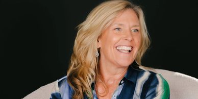 Smiling woman with blonde hair wearing a colorful blouse.