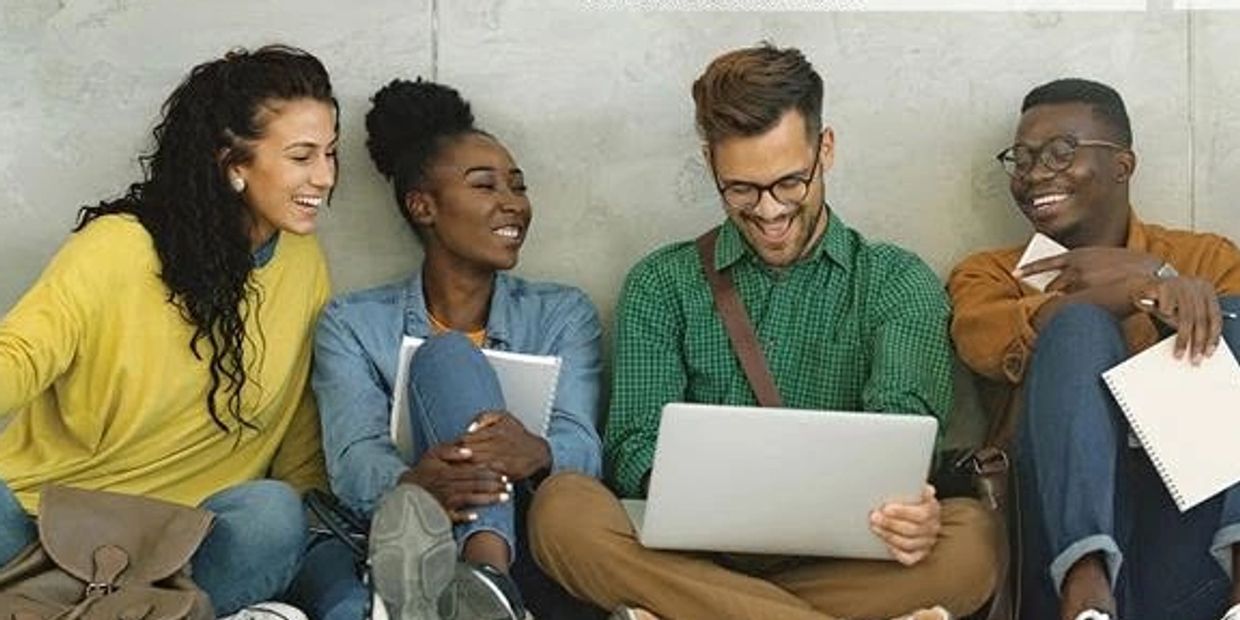 Four diverse friends sitting together, smiling and sharing a laptop screen.
