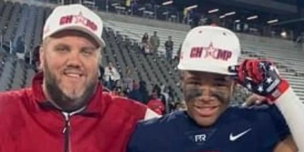 Two smiling men in sports gear and caps posing in a stadium.