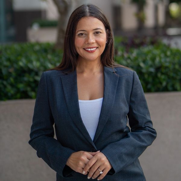 A smiling woman in a gray blazer outdoors.