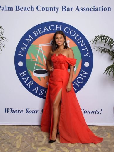 Woman in red dress posing at Palm Beach County Bar Association event.