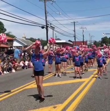 Cheerleaders perform with pink pom-poms in a street parade.