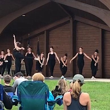 Group of dancers performing on an outdoor stage in black outfits.