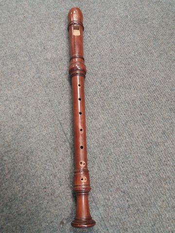 A wooden recorder lying on a carpeted floor.