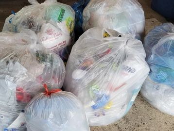 Several transparent garbage bags filled with household waste on the ground.