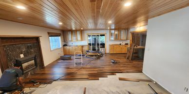 Person installing wooden flooring in a spacious room with wooden ceiling.