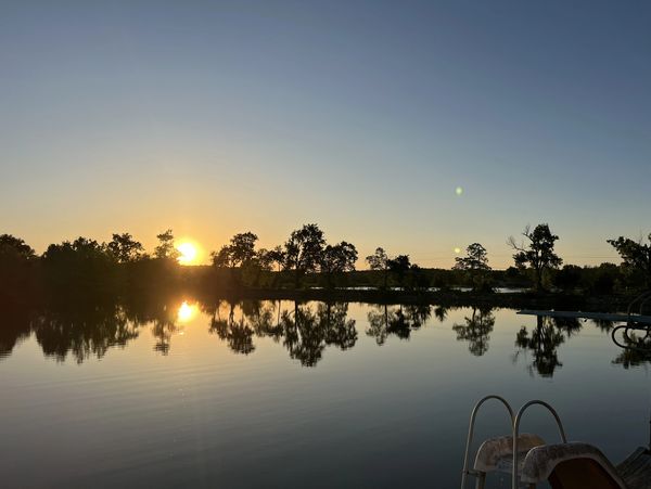 Sunset reflecting on a calm lake with trees silhouetted against the sky.