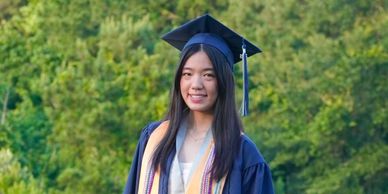 A young woman in graduation attire smiling outdoors.