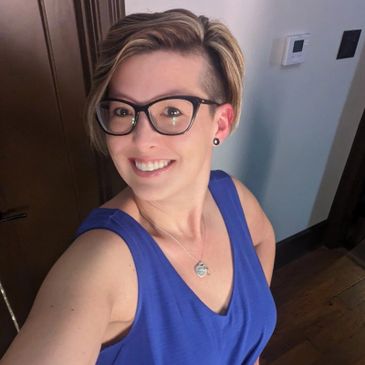 Smiling woman with glasses and short hair in a blue sleeveless top.