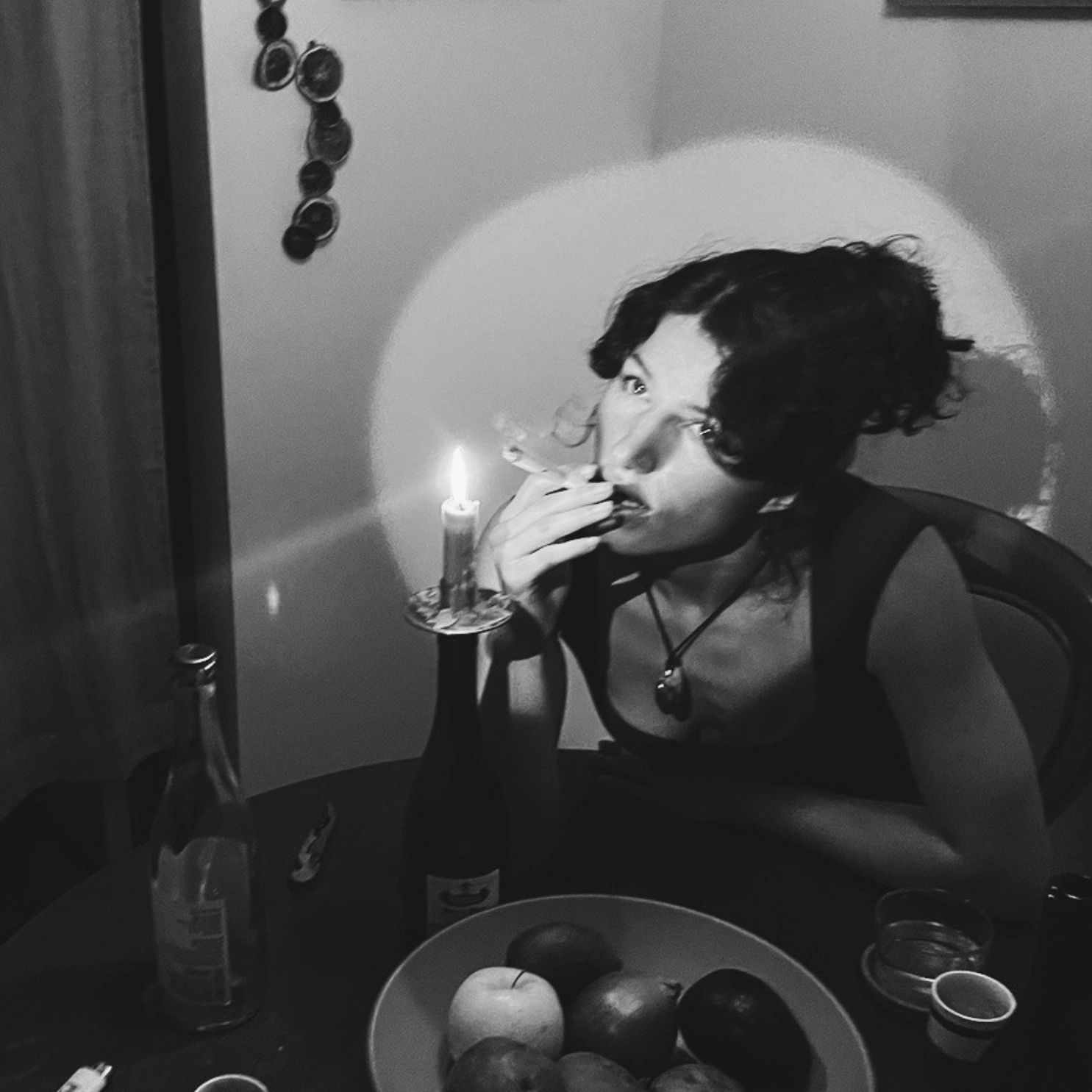 Black-and-white photo of a woman smoking by candlelight at a table.