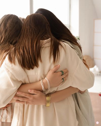 Three women sharing a warm group hug indoors.