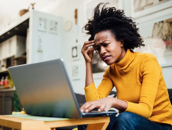 Woman in a yellow sweater looking confused while using a laptop.