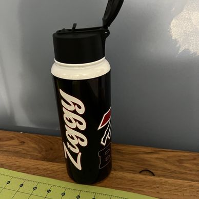 Black and white water bottle with flip-top lid on wooden surface.