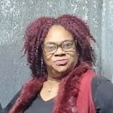 Woman with curly hair and glasses smiles confidently.