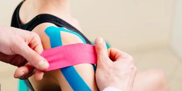 Applying colorful kinesiology tape on shoulder.