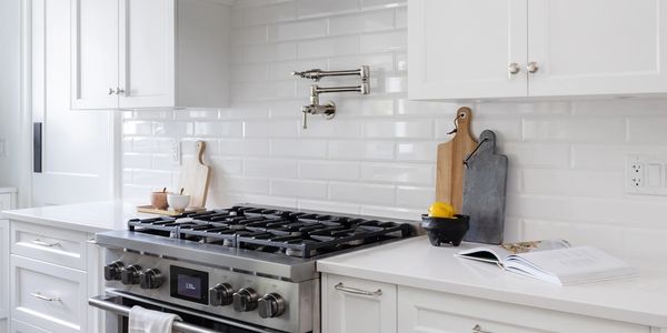 A modern white kitchen with a stainless steel gas range and a custom white range hood.
