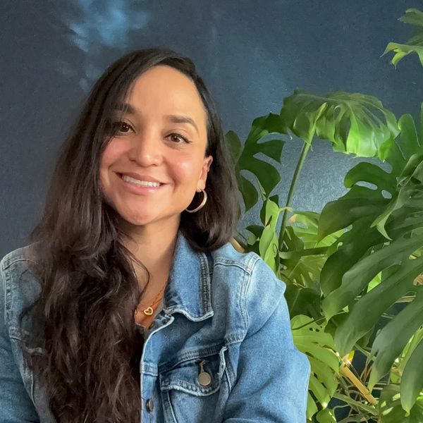 Janessa Jimenez, LMFT, smiling in a denim jacket beside a large monstera plant