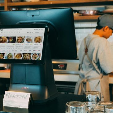 A reserved sign and digital menu screen at a restaurant counter with a worker in the background.