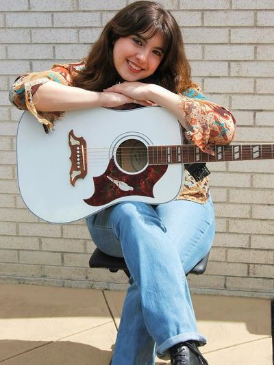 Young woman smiling while holding a white acoustic guitar.