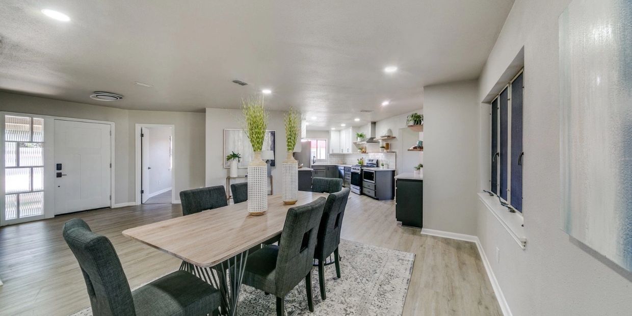 Modern dining room with wooden table and dark chairs next to an open kitchen.