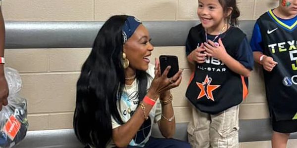 Woman happily talking to a young girl in sports jerseys.
