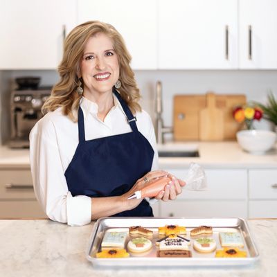 Smiling woman decorating cookies in a bright kitchen.