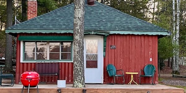 Cozy red cabin with outdoor seating and a grill on a wooden deck.