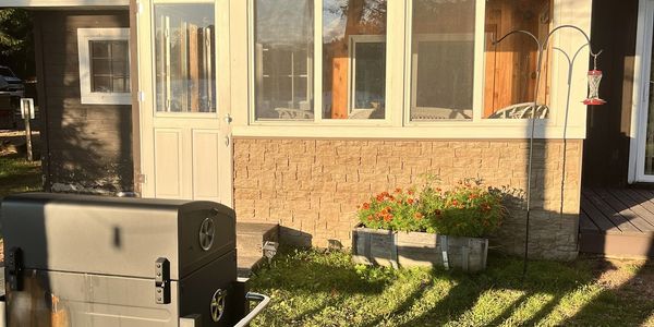 A backyard scene with a grill and flower boxes in sunlight.