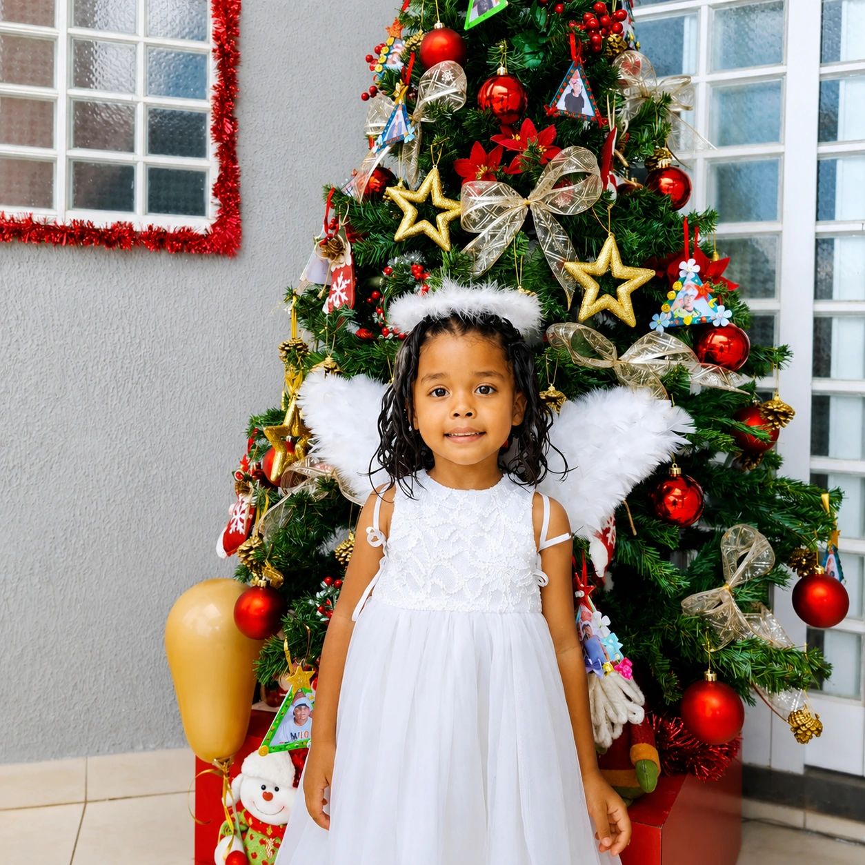 Little girl dressed as an angel stands by a decorated Christmas tree.