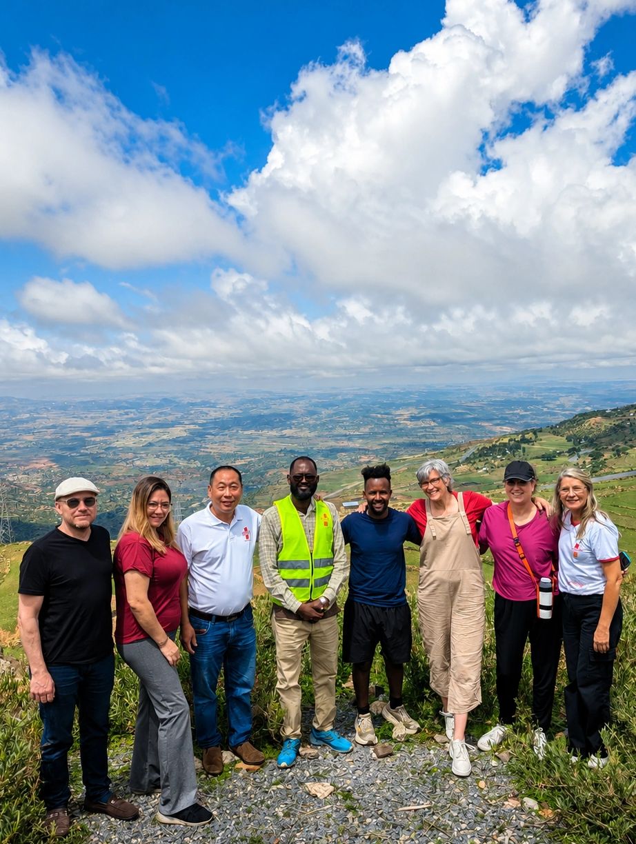 Group of eight people posing outdoors with a scenic mountain and valley view.