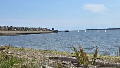 Calm seaside view with sailboats and distant coastline under a blue sky.