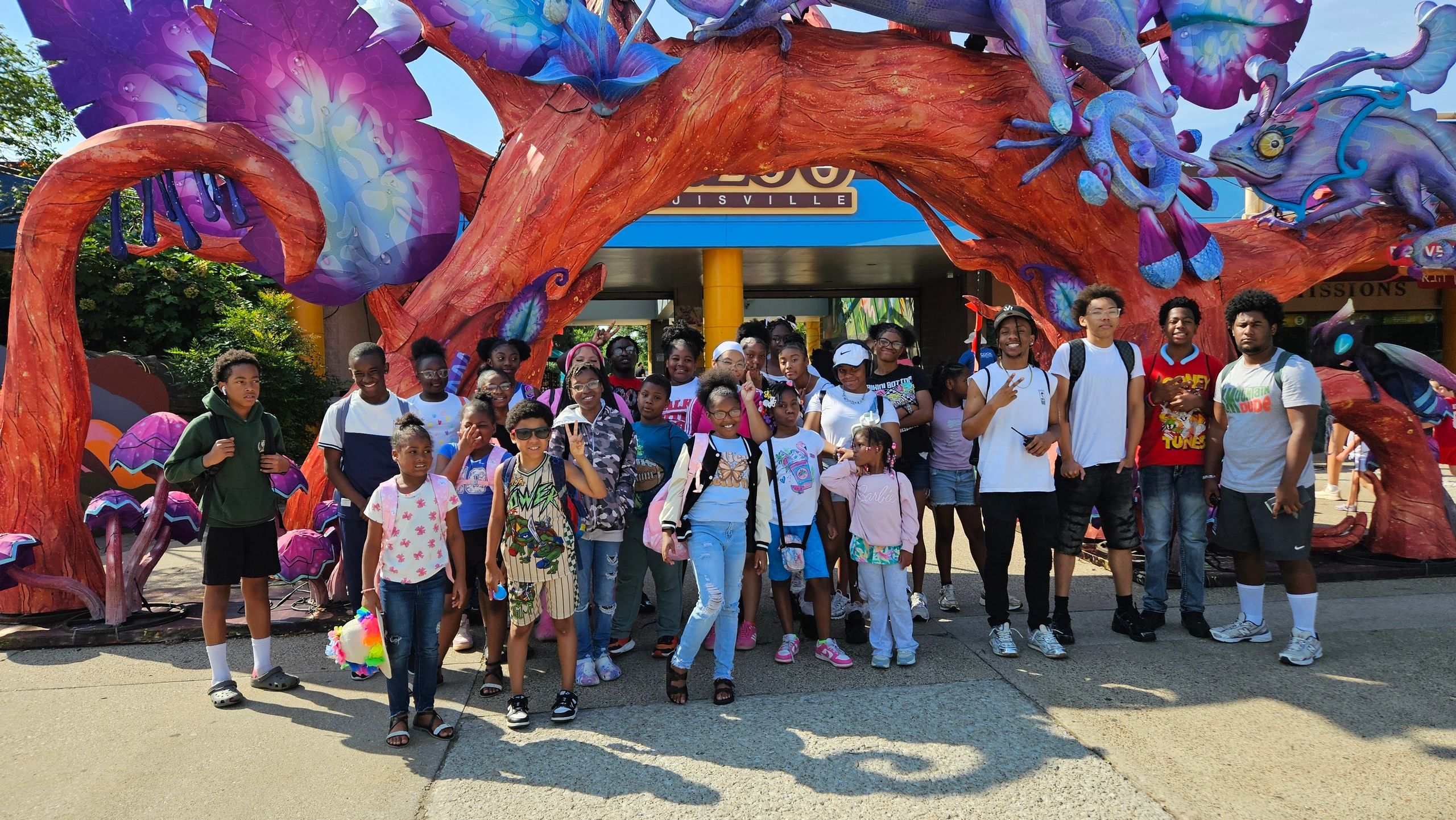 Large group of diverse children and adults pose under colorful arch.