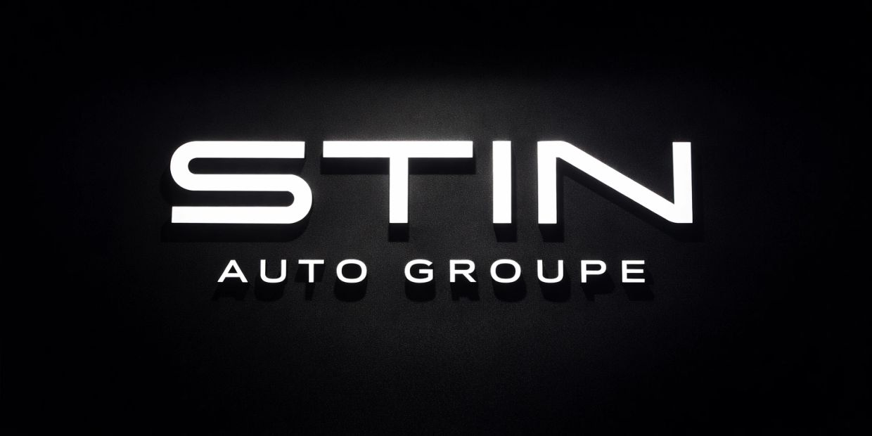 Illuminated STIN Auto Groupe sign on a dark background.